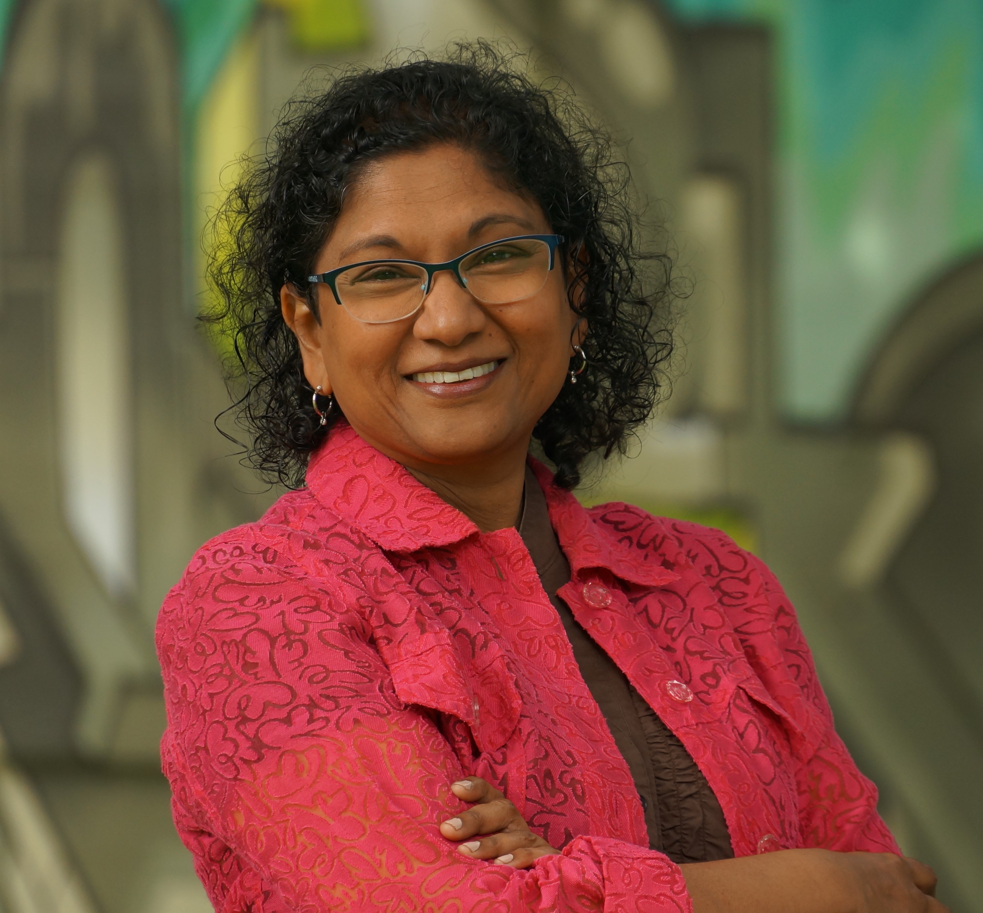 Head and shoulders photo of me (Me = curly, black-haired, brown-skinned woman wearing glasses, a pink laced jacket, brown shirt and a smile) Head and shoulders photo of me (Me = curly, black-haired, brown-skinned woman wearing glasses, a pink laced jacket, brown shirt and a smile)
